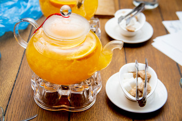 teaspoon of sea buckthorn and orange tea stand on tea burners, white and brown sugar on white saucers next to a wooden table in a cafe or restaurant