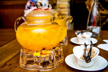 2 teaspoons of sea buckthorn and orange tea stand on tea burners, white and brown sugar on white saucers next to a wooden table in a cafe or restaurant