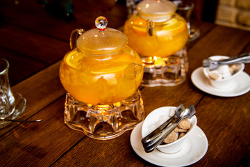 2 teaspoons of sea buckthorn and orange tea stand on tea burners, white and brown sugar on white saucers next to a wooden table in a cafe or restaurant
