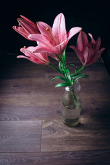 bouquet of pink lily flowers in the rays of light on a black background on a wooden rustic table in a glass bottle. fresh buds of a flowering plant close-up in a vase, copy space. studio shot