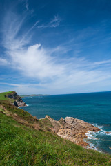 Sunny vertical landscape of rocky coast with blue sea and white clouds in northern Spain, Cantabria