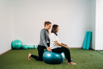 Pregnant woman doing fitness ball and pilates exercise with coach. Happy future mother preparing for childbirth.