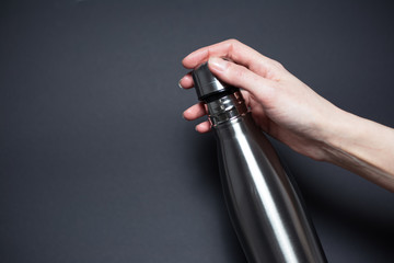 Close-up of hand holding ecologic steel thermo bottle for water, on black background