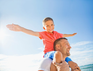 A Boy Piggybacking On His Dad Flying Like An Airplane With His Arms; Honolulu, Oahu, Hawaii, United States Of America