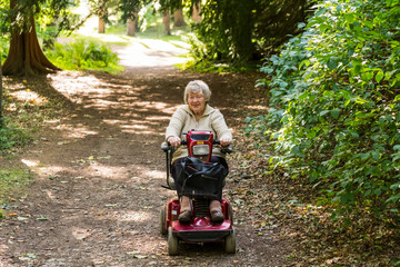 A Senior Woman Rides A Motorized Wheelchair Down A Trail In A Park; Yorkshire, England