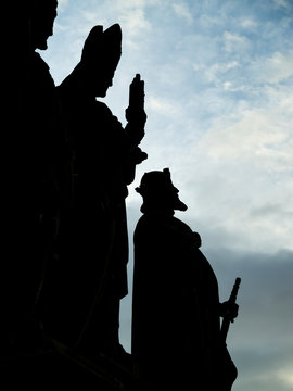 Silhouetted Statues Of Men In A Row On Charles Bridge With A Cloudy Sky In The Background; Prague, Czech Republic
