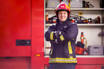 Image of smiling man firefighter in helmet on background of fire truck