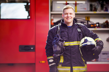 Fototapeta premium Photo of happy male firefighter with helmet in his hands against background of fire truck