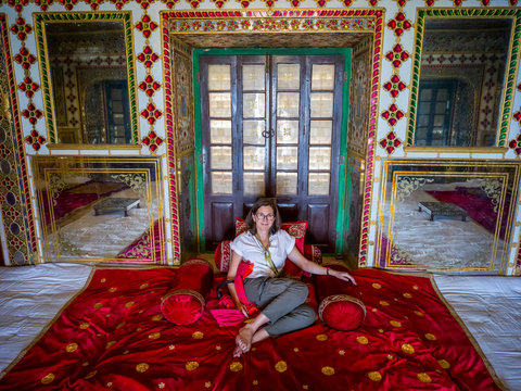 A female tourist sits on the luxurious red rug on the floor of the City Palace, Maharaja Sawai Mansingh II Museum, Mubarak Mahal; Jaipur, Rajasthan, India