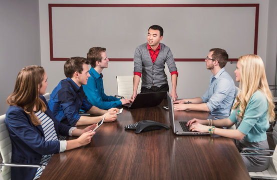 Young millennial business man speaking to a group of young professionals in a conference room in a place of business; Sherwood Park, Alberta, Canada