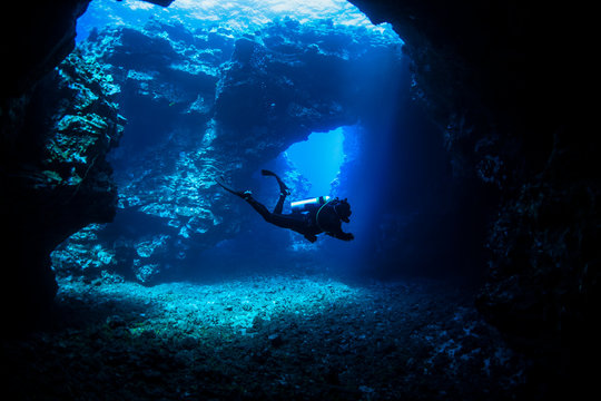 Scuba diver swims through lava arches with sun rays, Cathedrals dive site; Lanai City, Lanai, Hawaii, United States of America