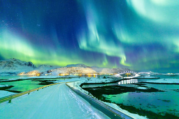 Aurora Borealis natural phenomenon on Lofoten Islands in Norway, Scandinavia, Europe. Night sky with northern lights over mountains and road reflected in fjord. Night winter landscape with aurora.
