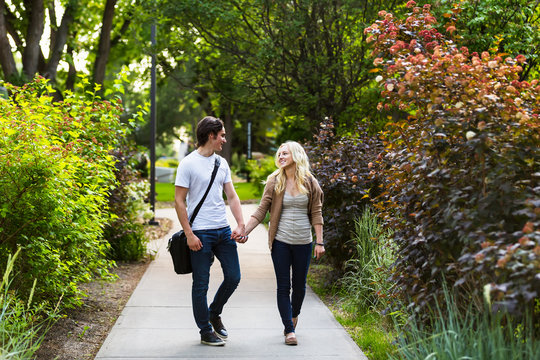 A young couple walking down a path on the university campus holding hands and talking; Edmonton, Alberta, Canada