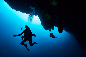 Scuba divers in the Great Blue Hole dive site on the Belize Barrier Reef. This site was made famous by Jacques Cousteau, who declared it one of the top five scuba diving sites in the world; Belize