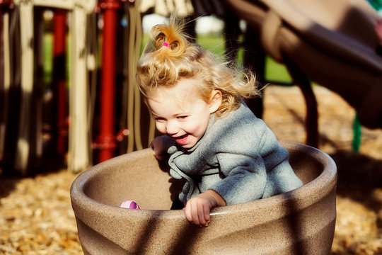 A cute young girl spinning in a saucer on a playground during the fall season; Spruce Grove, Alberta, Canada