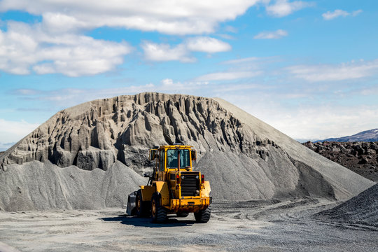 A large wheel loader heavy equipment machine is parked in front of a gravel pile in the mountain landscape; Iceland