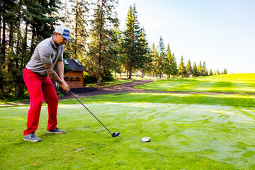 A male golfer lines up his shot as he prepares to tee off using a driver to drive the ball down the fairway of a golf course in the early morning; Edmonton, Alberta, Canada