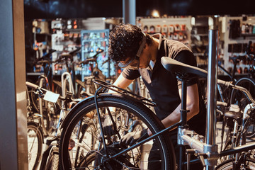 Obraz premium Pensive diligent master in protective glasses is fixing bicycle at workshop.