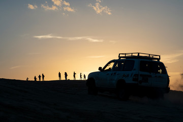 Fototapeta na wymiar 4x4 car on top of sand dune at sunset with people watching the setting sun