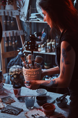 Young attractive painter is holdind jar with brushes in her own cozy workshop.