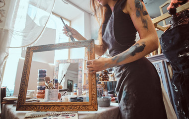 Young talented painter is restourating old frame in her own workshop.