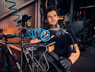 Fototapeta na wymiar Handsome talented master is fixing bicycle at his own workshop using pneumatic tool.