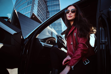 Young attractive women is posing in her new car. She is wearing red jacket and sunglasses.