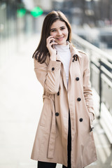 Portrait of a woman wearing a white coat calling on phone and looking at side on the street in winter