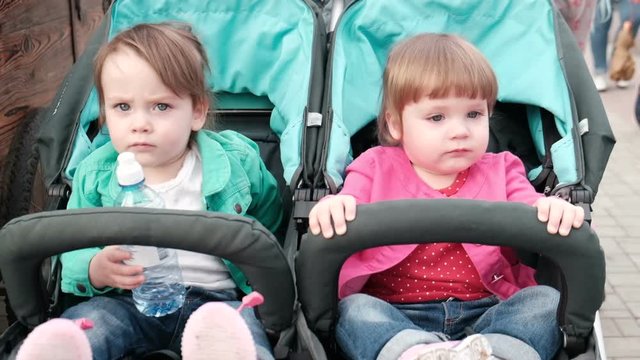 Little sisters twins sitting in a stroller together close up