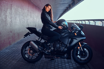 Attractive brave woman is sitting on her motobike in tunnel. She is holding helmet.