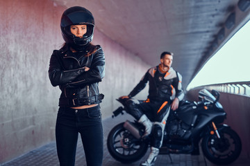 Couple of young bikers is relaxing in quiet tunnel with their motobike. Girl is wearing helmet. Man...