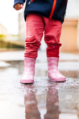 Child standing with pink rubber boots in puddle. Kind steht mit rosa Gummistiefeln in Wasserpfütze.