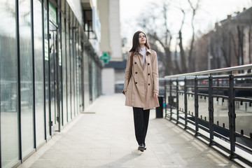 Obraz premium Excited young woman wearing coat and eyeglasses using mobile phone while walking through city street
