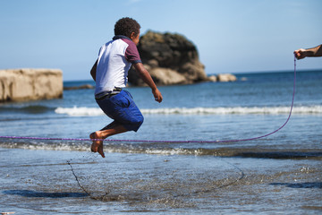 A child jumping over a skipping rope on a beach on a sunny day