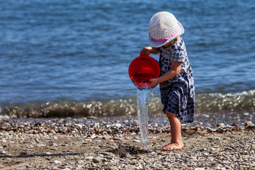 A child on the beach in the summer playing with a bucket of water