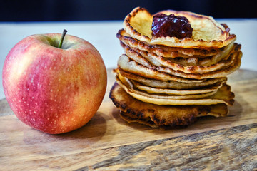 Pancakes with jam on the kitchen board. A red apple lies next to the pancakes. Still life on the kitchen table
