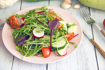Salad with spring greens, cucumbers, tomatoes and radishes. Green salad with arugula and chard. Veggie cuisine, salad with vegetables on a pink plate on a wooden background