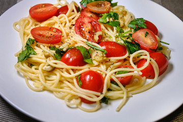 Pasta with tomatoes. Plate with spaghetti and cherry tomatoes on the table. Pasta decorated with leaves of parsley and cilantro.