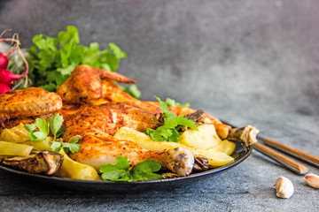 Baked chicken with garlic, spices and grilled vegetables lies on a black plate, next to cutlery and fresh vegetables, a paleo diet. Copy space