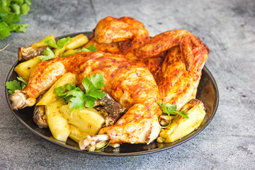 Chicken tobacco national dish of Georgian cuisine. Baked chicken with garlic and grilled vegetables on a black plate on a stone background, next to fresh greens and vegetables.  Copy space