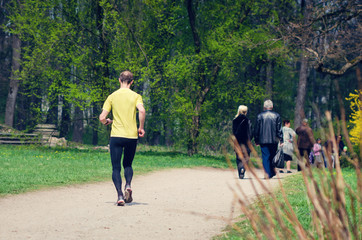 Rear view, the athlete runs on the road in the park in spring