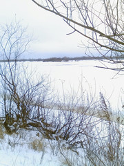 Bare bushes on the shore, ice and snow on a frozen river on the second day of spring.                  