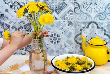 Little hands of child bunch of yellow flowers from dandelion on background from pattern tiles.
