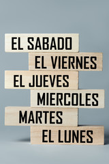 A list of wooden blocks lying on top of each other with a list of six-day working week days in Spanish, in the translation of the word: saturday, friday, thursday, wednesday, tuesday, monday