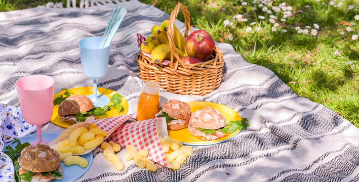 A basket of fruit and sandwiches for a picnic outdoors in the park. Nice sunny day and summer lunch.