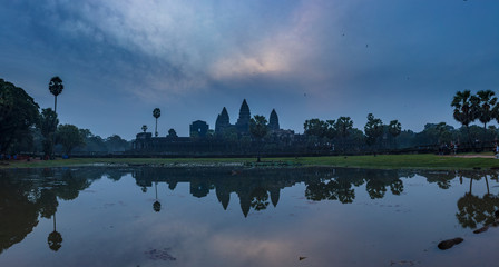 Angkor Wat temple reflected in a pond during an overcast sunrise.