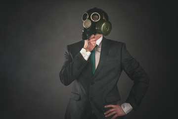 Man in a gas mask and suit is thinking about pollution of environment on a gray background.