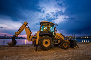 Amazing view at yellow excavator with a shovel at a construction site in a beautiful twilight