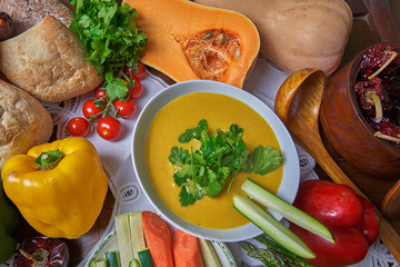 Aerial still life. Cream of carrots and potatoes. Craft bread, tomatoes, peppers, zucchini, carrots, dried peppers, coriander and pumpkin. 
