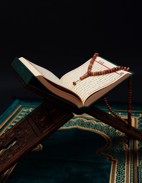 Islamic Holy Book Quran on wood carving rahle with rosary beads and prayer rug on black background. Kuran the holy book of Muslims. Ramadan concept.